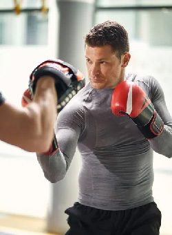 Close-up of a muscular, Caucasian male with brunette hair working mitts for muay thai.